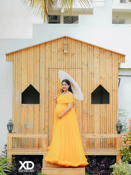 A beautiful solo portrait of the mother-to-be in a yellow gown, holding a paper umbrella in a rustic setting.