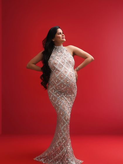 A powerful and confident pose. The mom-to-be looks up with a hopeful expression, her stunning sequined gown creating a striking silhouette against the red background.
