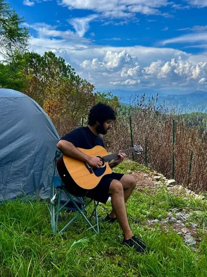 A musician plays his guitar against a backdrop of rolling hills and a brilliant blue sky at our Renz Himalayan Retreat. Our retreats offer a perfect setting for inspiration and collaboration.