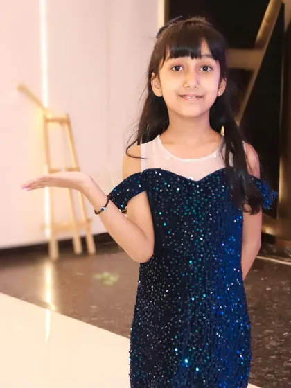 A young girl in a sparkling blue dress poses elegantly for a portrait. We guide children into poses that are both natural and photogenic.