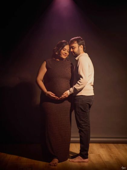 In this full-length portrait, the couple stands together in a soft spotlight. It’s a quiet, tender moment that shows their unity and shared excitement for their growing family.