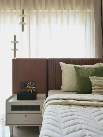 A closer look at the parent's bedroom, highlighting the textures of the fluted headboard and the quilted bedspread. The olive green cushions add a touch of color to the serene rose brown and beige palette.