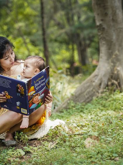 A mother reads a storybook to her baby in a peaceful, wooded setting.