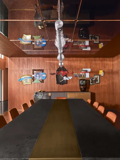 The dining room at Baid Residence, where a reflective ceiling mirrors the long dining table and a collection of art and objects. The space is a curated blend of international design and personal artifacts.