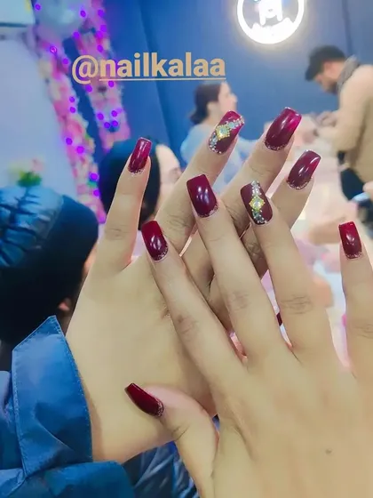 A deep, glossy maroon polish on square-shaped nails. This set is enhanced with a single accent nail featuring an intricate gold and crystal design, showing how to elevate a classic manicure.
