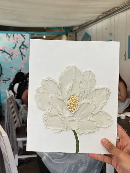 A close-up of a finished white floral piece. The simplicity of the color allows the rich texture and gold leaf to really shine.