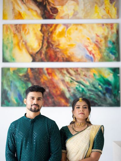 A modern engagement portrait of a couple standing before a vibrant abstract painting, their traditional attire creating a beautiful contrast.
