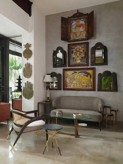 The entrance area of the living room, where a wall is adorned with old Vaishnavite Tanjore paintings juxtaposed with Pharaonic mirrors from Egypt. This eclectic mix immediately establishes the home's multicultural and personal aesthetic.