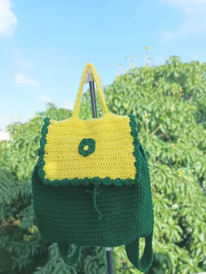 A clear product shot of the green and yellow backpack, showing the scalloped edge detail on the flap and the drawstring closure.