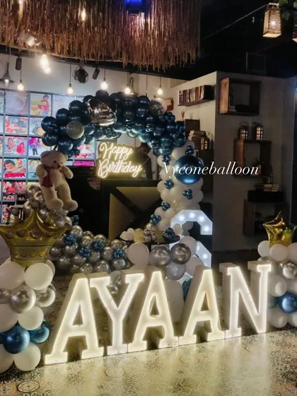 Personalize your child's party with large, light-up marquee letters spelling their name. Here, 'AYAAN' is the star of the show, complemented by a blue and silver balloon ring decoration.