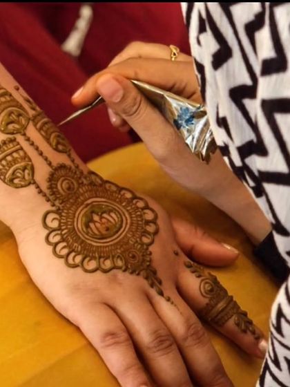 A close-up of the mehendi application process. You can see the cone in action as I create a beautiful lotus and jhumka design, applying the paste with precision and care.