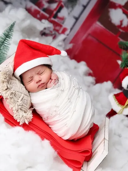A sweet newborn nestled in a sleigh, with a miniature Santa Claus figure adding to the Christmas magic.