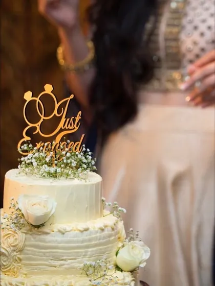 A classic two-tiered cake for a "Just Engaged" celebration, adorned with delicate baby's breath and fresh white roses. This elegant design is perfect for engagement parties, anniversaries, or intimate weddings.