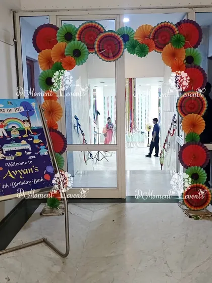 The welcome area for the "Colors of Joy" Art & Craft party. An arch made of colorful paper fans and a themed welcome sign greet the guests.