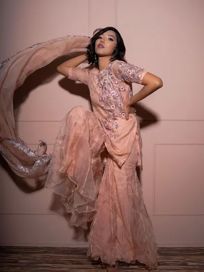 A dynamic and energetic pose, with the model kicking up her leg to show the movement of the sharara pants and dupatta. This shot is full of life and high-fashion energy.
