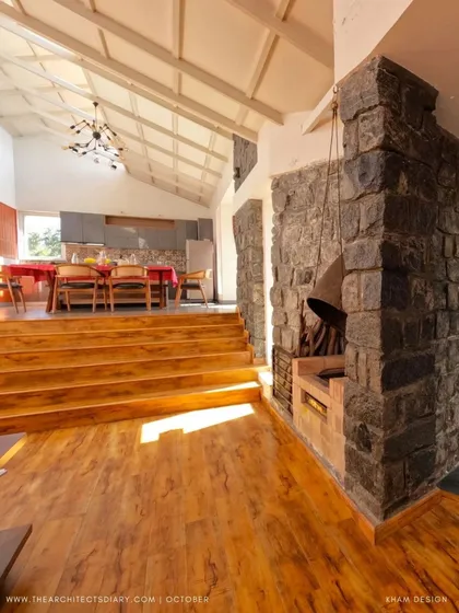 The massive stone fireplace serves as an anchor for the main living area, providing warmth and a strong textural element. The steps lead up to the open-plan kitchen and dining space, showcasing the home's multi-level layout.