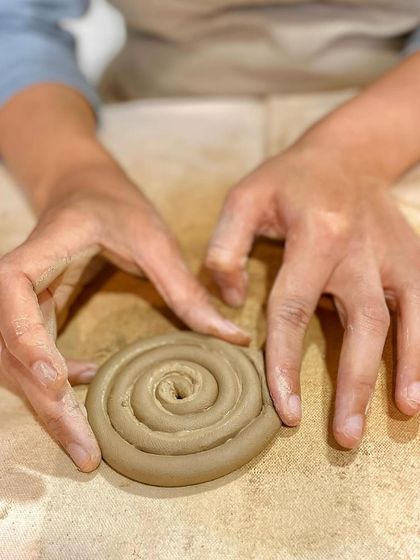 The coiling technique involves rolling out long ropes of clay and building them up, layer by layer. Here, a student is starting the base for a coiled pot.