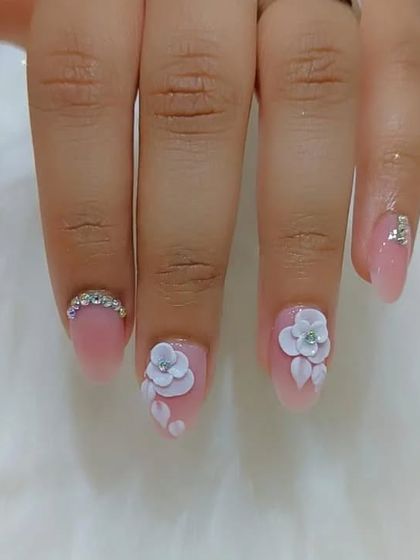 This image showcases the delicate balance of 3D art and simple elegance, with sculpted flowers on some nails and rhinestone accents on others.
