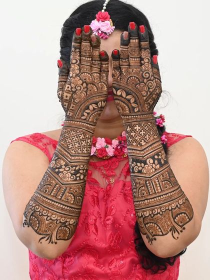 A shy and sweet pose from a bride, her face hidden behind her fully decorated hands. This classic shot highlights the intricacy of the full-coverage mehendi.