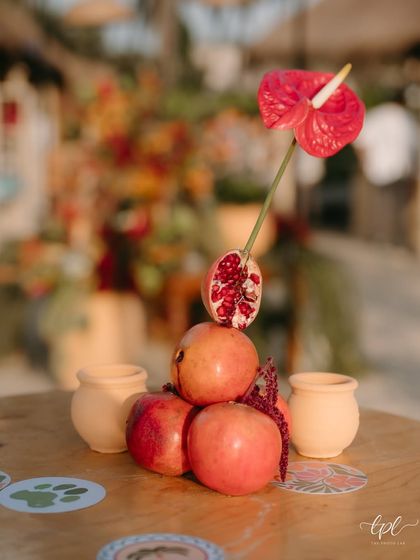 A small, artistic arrangement of pomegranates and an anthurium flower, part of the creative decor for the tropical beach event.