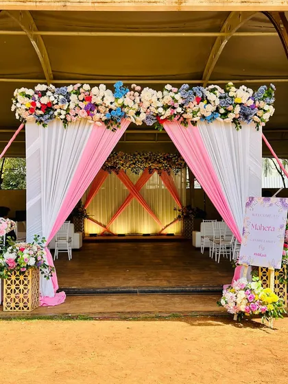 The entrance to the Mayra ceremony, featuring a lovely arch of multicolored flowers and elegant pink and white drapes.
