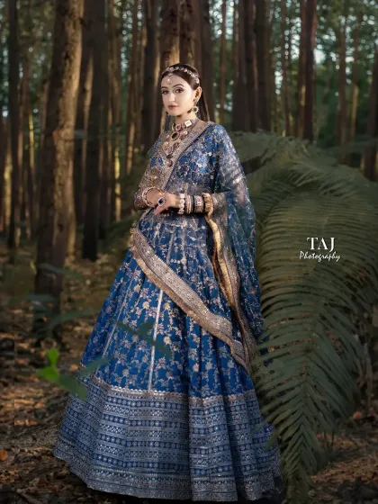 A fairytale bridal portrait in a forest setting. The bride's royal blue lehenga stands out beautifully against the natural, woody background.