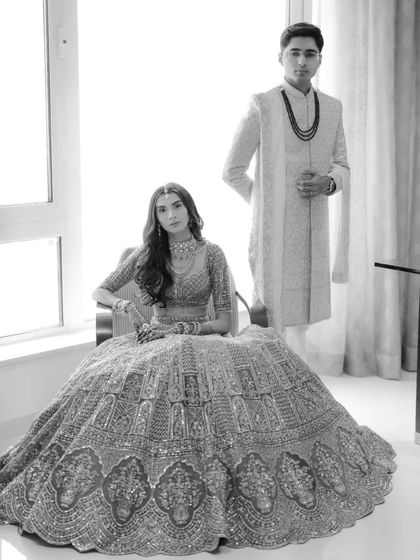 A classic black and white portrait of the couple, the bride seated while the groom stands, creating a formal and elegant composition.