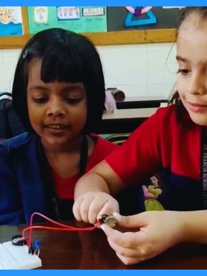 Two very young students work together on a simple circuit with a battery and breadboard. Their gentle handling of the components shows that learning electronics can be accessible and engaging for all ages.