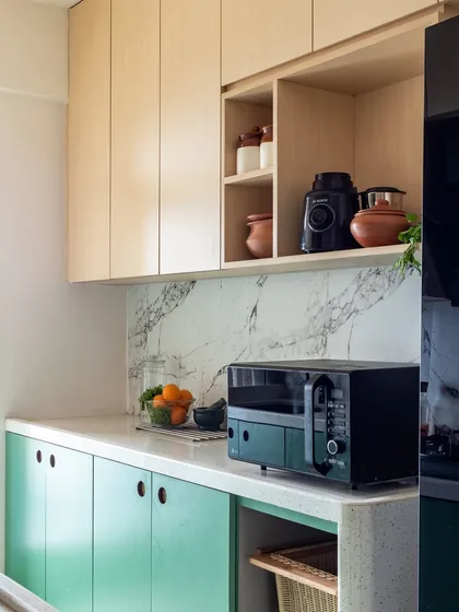 The kitchen features an arched doorway, creating a soft and inviting transition from the dining area. The green lower cabinets add a pop of color, while the circular cutouts for handles are a unique, minimalist detail.