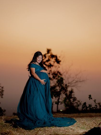A stunning silhouette against a sunset sky. This teal maternity gown with its long train is perfect for creating dramatic and beautiful shots at dusk.