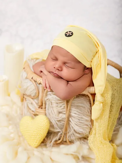 A full portrait of a newborn sleeping in a basket, with soft lighting from prop candles creating a warm and gentle atmosphere.
