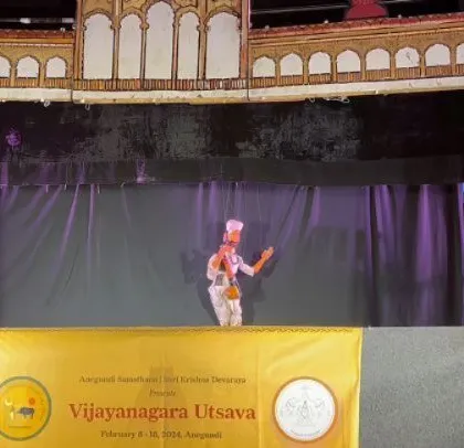 A single puppet takes the stage, holding the attention of the entire audience. This shot highlights the intricate design of the stage backdrop, inspired by Vijayanagara architecture.