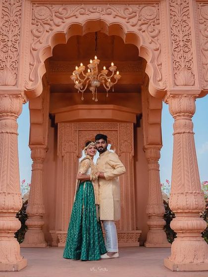 A full-length portrait of the couple framed by the ornate pillars of the palace. This shot captures both the couple's elegant outfits and the stunning details of the royal architecture.