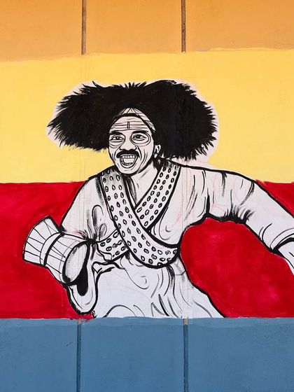 This expressive mural captures a character from Kannada culture, painted against the backdrop of the state flag, fostering a sense of pride.