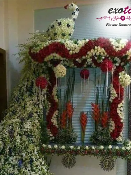 An extravagant floral peacock sculpture for a Ganpati mandap. The peacock's body and cascading tail are made from thousands of red and white flowers, creating a truly spectacular piece of art.