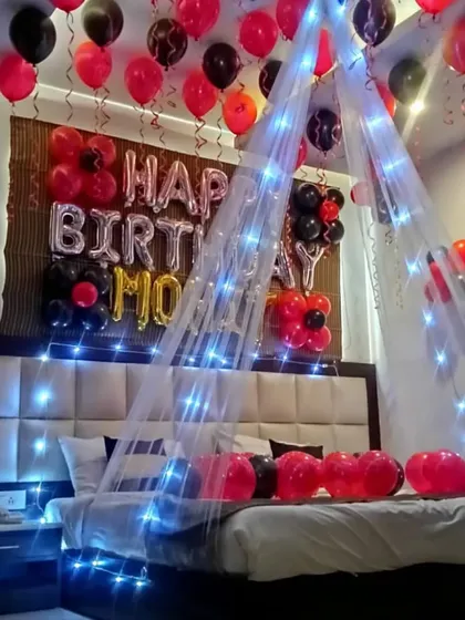 A birthday room decoration featuring a canopy with blue fairy lights. The red and black balloons and "Happy Birthday Mom" foil letters make it a special surprise.