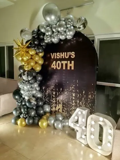 A sophisticated 40th milestone birthday setup. The decor features a custom black and gold backdrop, a stylish balloon garland, and large marquee numbers, creating a classy and memorable spot for photos.