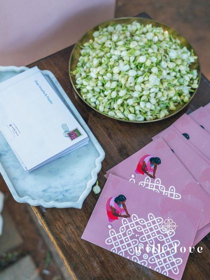 A guest message station at a summer wedding, with custom kolam-themed cards and a bowl of fragrant jasmine buds.