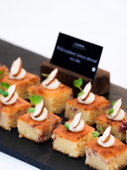 Our wild raspberry lemon almond cake, served as bite-sized canapés at a polo match high tea. These little squares are moist, flavourful, and elegantly garnished with an almond slice and microgreens.
