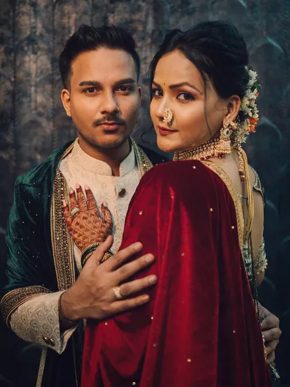 A royal and romantic couple portrait. The groom holds his bride, who is draped in a rich red velvet shawl, and she looks back at the camera with a powerful gaze.