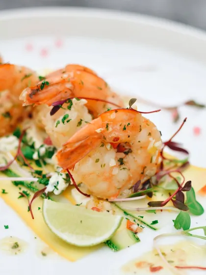 A close-up of perfectly cooked garlic prawns, garnished with fresh herbs. This bright and fresh shot is designed to make the dish look appetizing and highlight its quality ingredients.