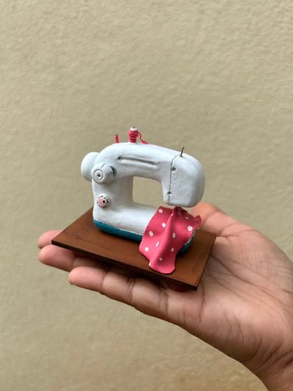 A close-up of the hand-sculpted sewing machine. It sits on a small wooden base, ready to be displayed.