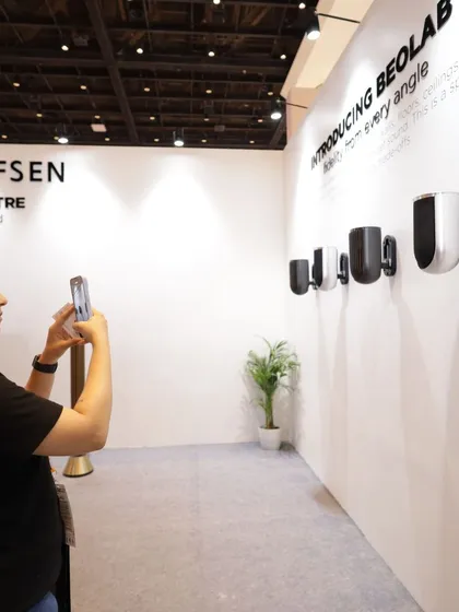 A visitor photographs a display of stylish, wall-mounted speakers from Bang & Olufsen, capturing the blend of high-end audio and sophisticated design.