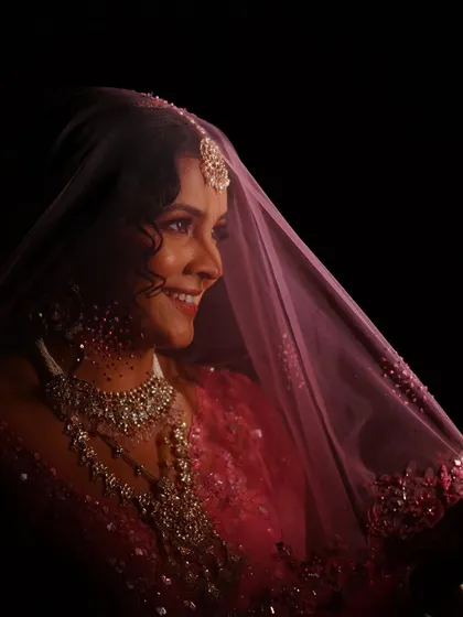 A classic bridal portrait under the veil. The soft lighting and her gentle smile are enhanced by a makeup look that is all about natural radiance and timeless elegance.