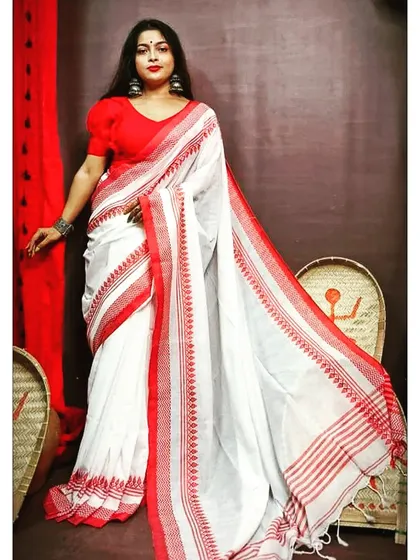 This is the iconic 'lal paar' saree, a must-have for Durga Puja. The classic white cotton saree with a simple red border is timeless. I rent it with a pre-stitched red puff-sleeve blouse to give you a complete, ready-to-wear traditional Bengali look.