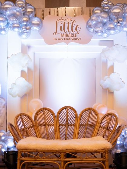 The elegant peacock chair, a perfect throne for the mom-to-be. It’s set against a backdrop that reads 'Our Little Miracle is on the way', framed by soft, glowing clouds.
