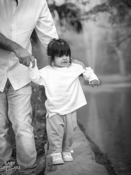 A father holds his daughter's hand as she carefully walks along a ledge. Black and white enhances the sense of trust and connection.