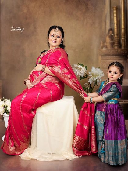 A heartwarming family portrait from a traditional shoot. The daughter playfully tugs on her mother's saree, adding a touch of candid joy to this beautifully styled, classic image.