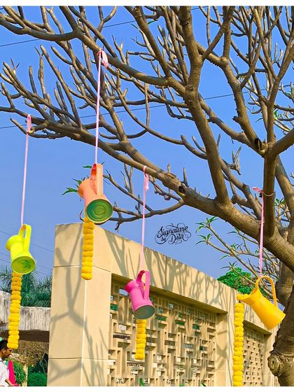 Creative hanging decor using colorful watering cans and strings of marigolds, adding a unique and whimsical touch to the trees.