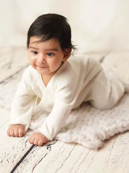 A full shot of the baby on his tummy, looking off to the side with a sweet smile. The rustic wood floor and simple blanket create a timeless look.
